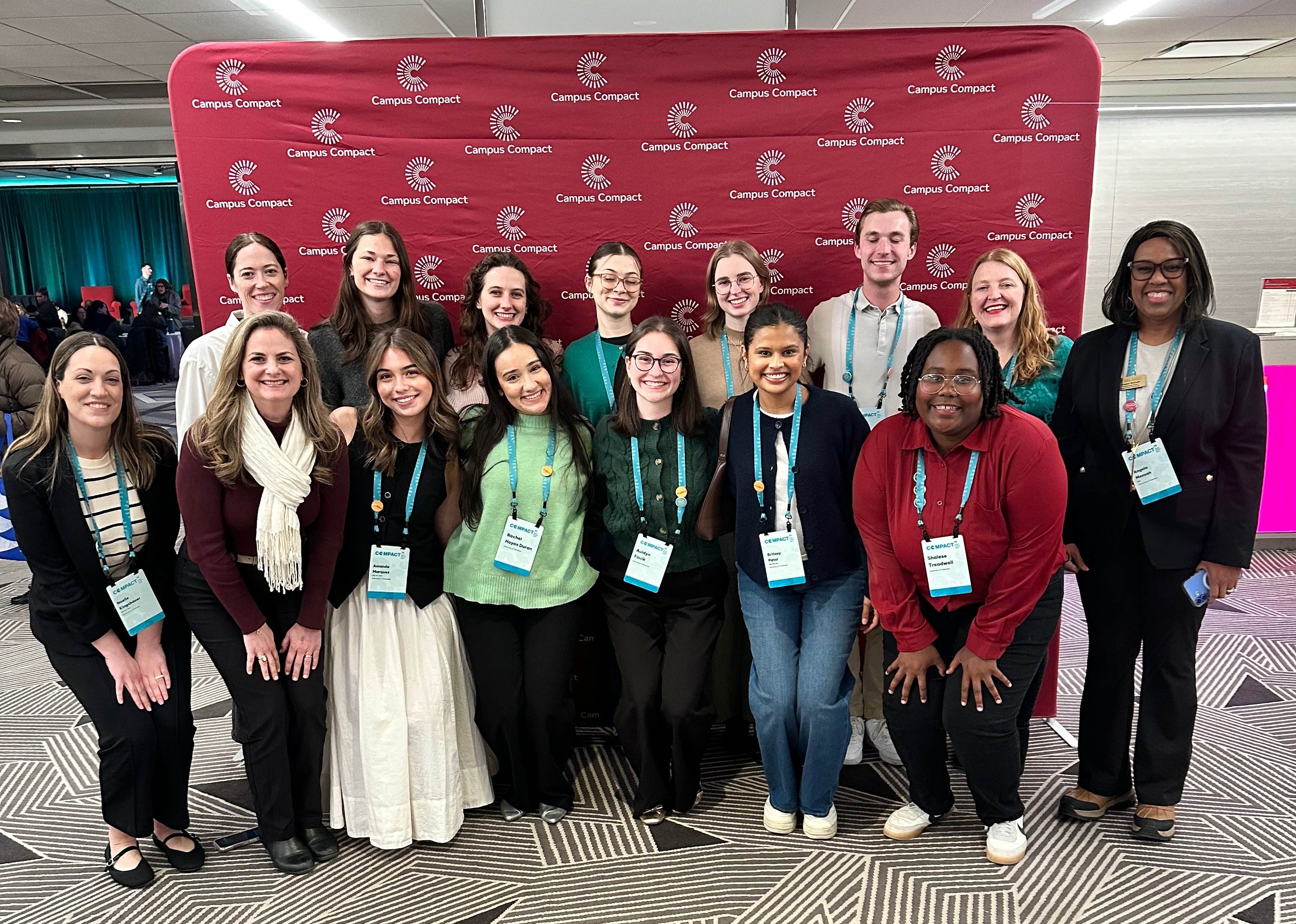 Service Learning staff, faculty members, and Volunteer Action Center students pose for a group photo in front of a Campus Compact conference banner.